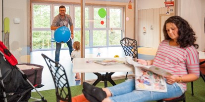 Familienhotel - Suiten mit extra Kinderzimmer - Bayern - Papa dribbelt mit der Kleinen im Turnhällchen, Mama entspannt endlich mal im Elternbistro - Familotel Landhaus zur Ohe