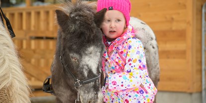 Familienhotel - Spielplatz - Großarl - Mädchen kuschelt mit dem Pony - Familienhotel Auhof