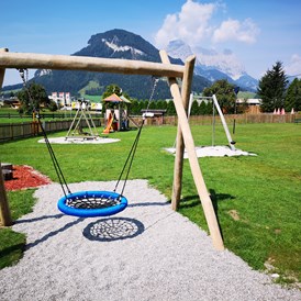 Kinderhotel: Freie Benützung der unmittelbar angrenzenden Spielwiese mit Nestschaukel, Seilrutsche, Spielturm und Trampolin - Hotel babymio