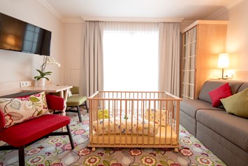 Kinderhotel: Familienzimmer - Wohnbereich mit Gitterbett - Hotel Felsenhof