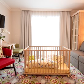 Kinderhotel: Familienzimmer - Wohnbereich mit Gitterbett - Hotel Felsenhof