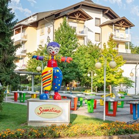 Kinderhotel: Maskottchen Sonnelino mit Hotel und Pit Pat im Hintergrund - Baby + Kinderhotel Sonnelino